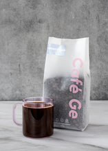 Cargar imagen en el visor de la galería, Bosa de cafe americano con taza transparente a lado
