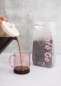 Gif con una jarra que vierte cafe en una taza rosa transparente a lado bolsa transparente de cafe en grano tipo americano